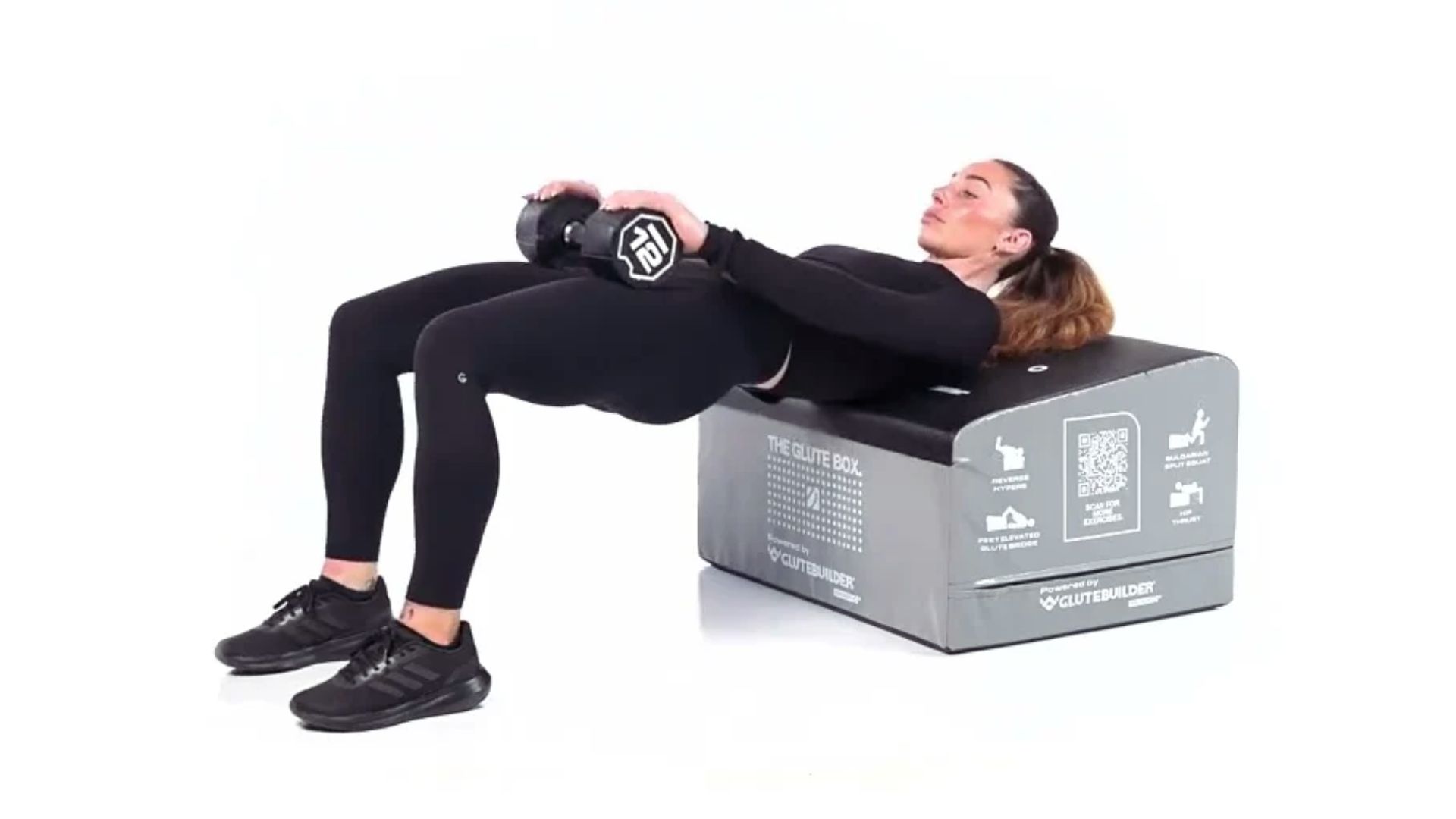 Woman performing hip thrust exercise on a box with a 12 kg dumbbell. She's in athletic wear, demonstrating strength and focus in a gym setting.