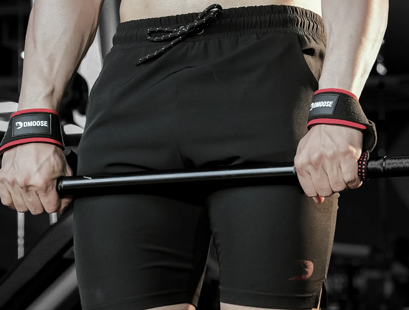 A man wearing black shorts and red wristbands lifts a barbell, showcasing strength and focus in a gym setting.