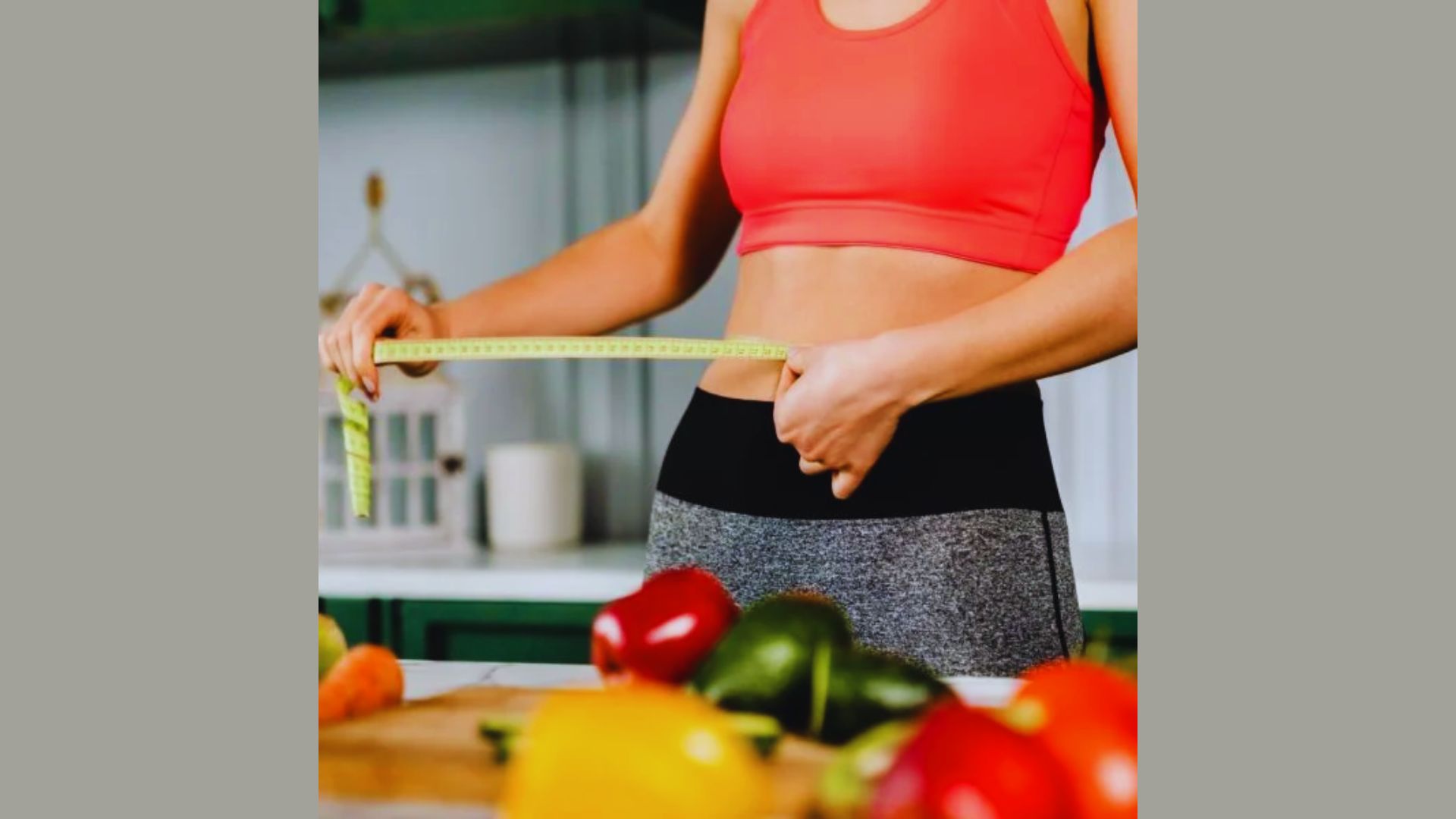 A person in a red sports top measures their waist with a tape measure in a kitchen. Various colorful vegetables are in the foreground, suggesting a focus on health and fitness.