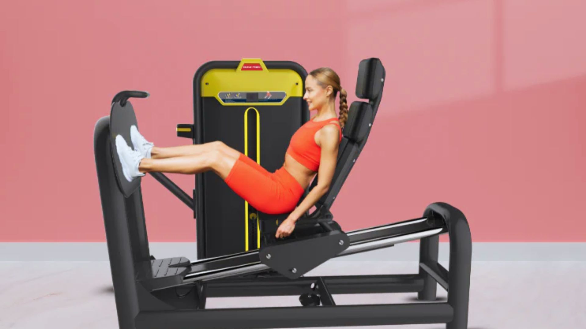 A woman in a bright orange workout set is using a leg press machine against a pink background. She appears focused and determined.