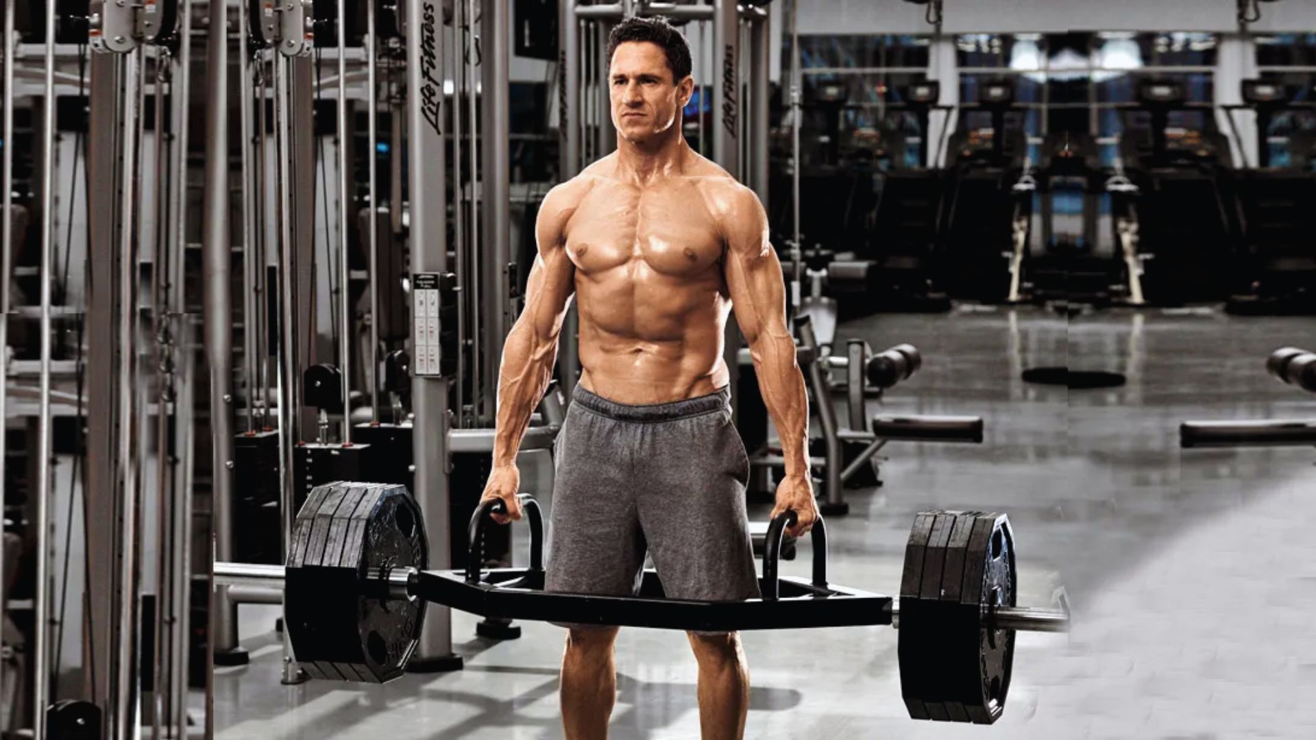 Muscular man performing deadlift with a hex bar in a modern gym. He shows determination and strength, surrounded by various exercise equipment.