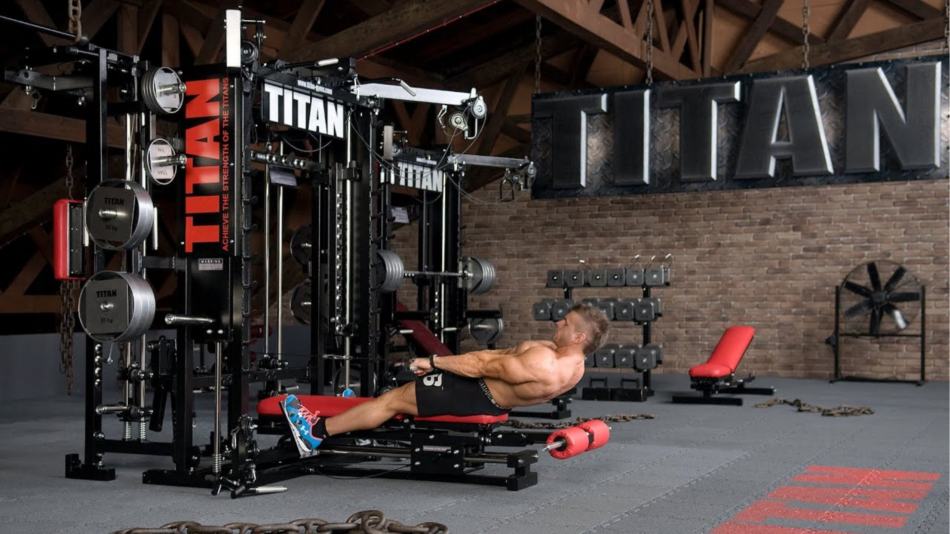 A muscular man exercises using a cable machine in an industrial-style gym. A large "Titan" sign is on the brick wall, conveying strength and focus.