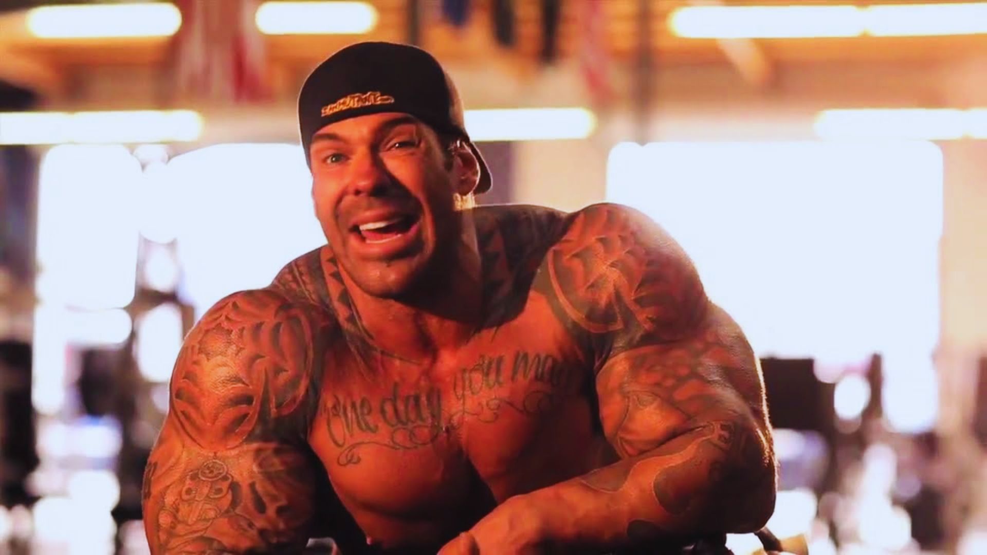 A smiling man with tattoos and a hat, exuding a cheerful and confident demeanor.