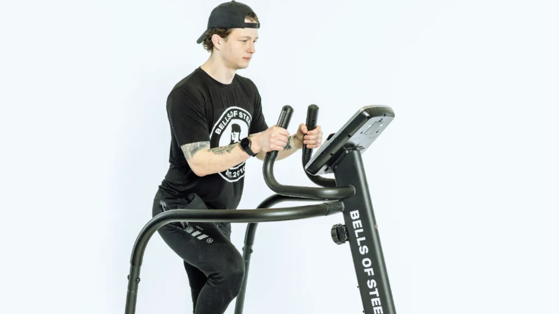 Young man in a black cap and workout clothes uses a stair stepper machine. The mood is focused and energetic, promoting fitness and exercise.