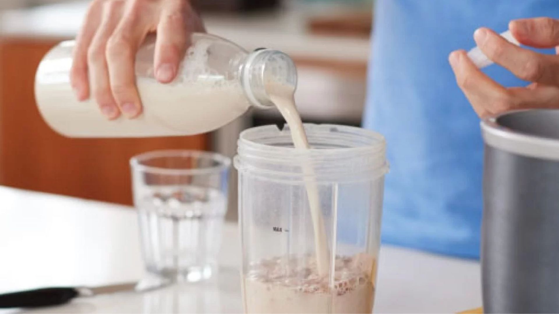 A person pouring milk into a blender, preparing ingredients for a smoothie or beverage.