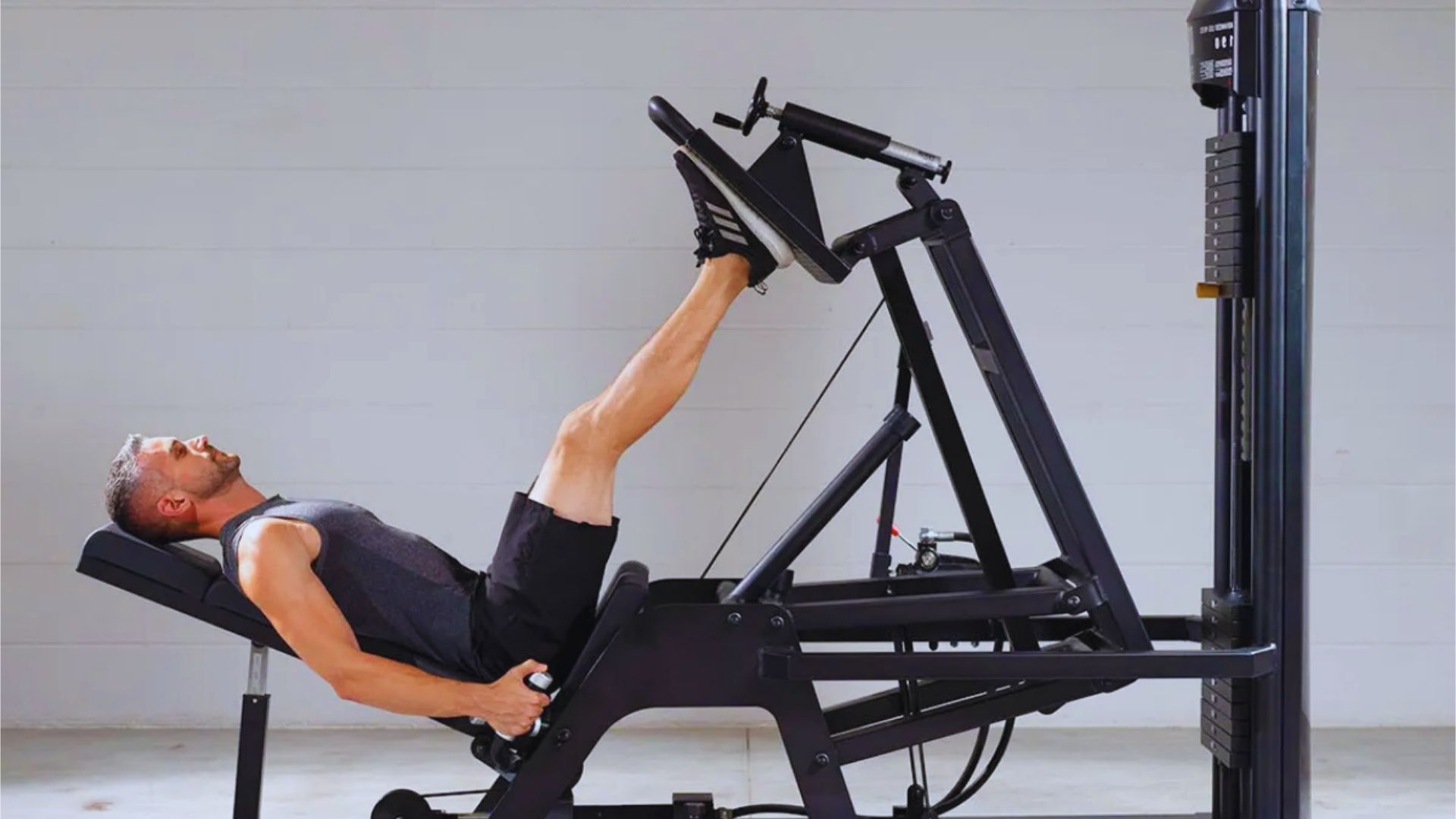 A man in athletic wear uses a leg press machine at the gym, appearing focused and determined. The environment is minimalist with neutral tones.