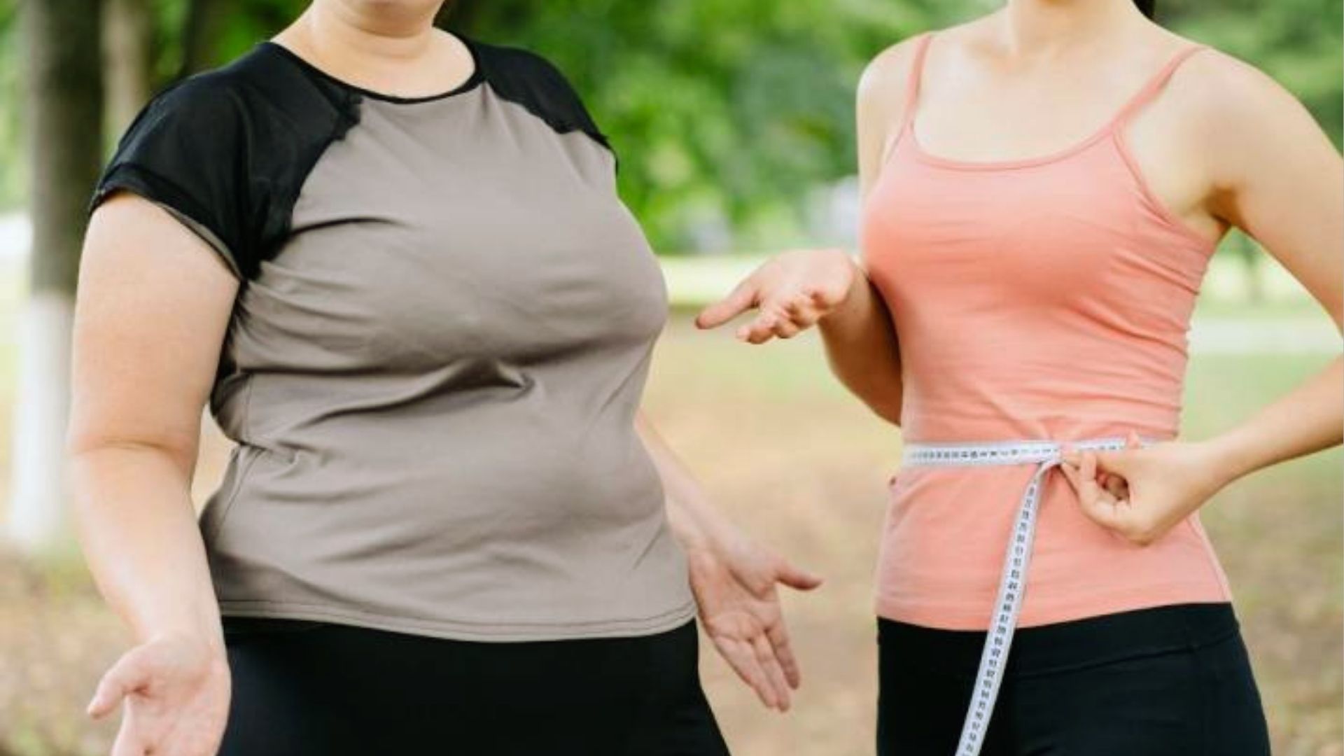 Two women outdoors, one in a gray shirt and the other in a pink top. The woman in pink measures her waist with tape, suggesting weight comparison.