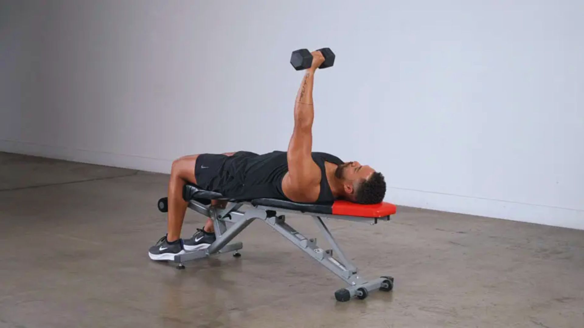 A person in athletic wear performs a dumbbell bench press on an incline bench in a minimalist gym. The scene conveys focus and strength.