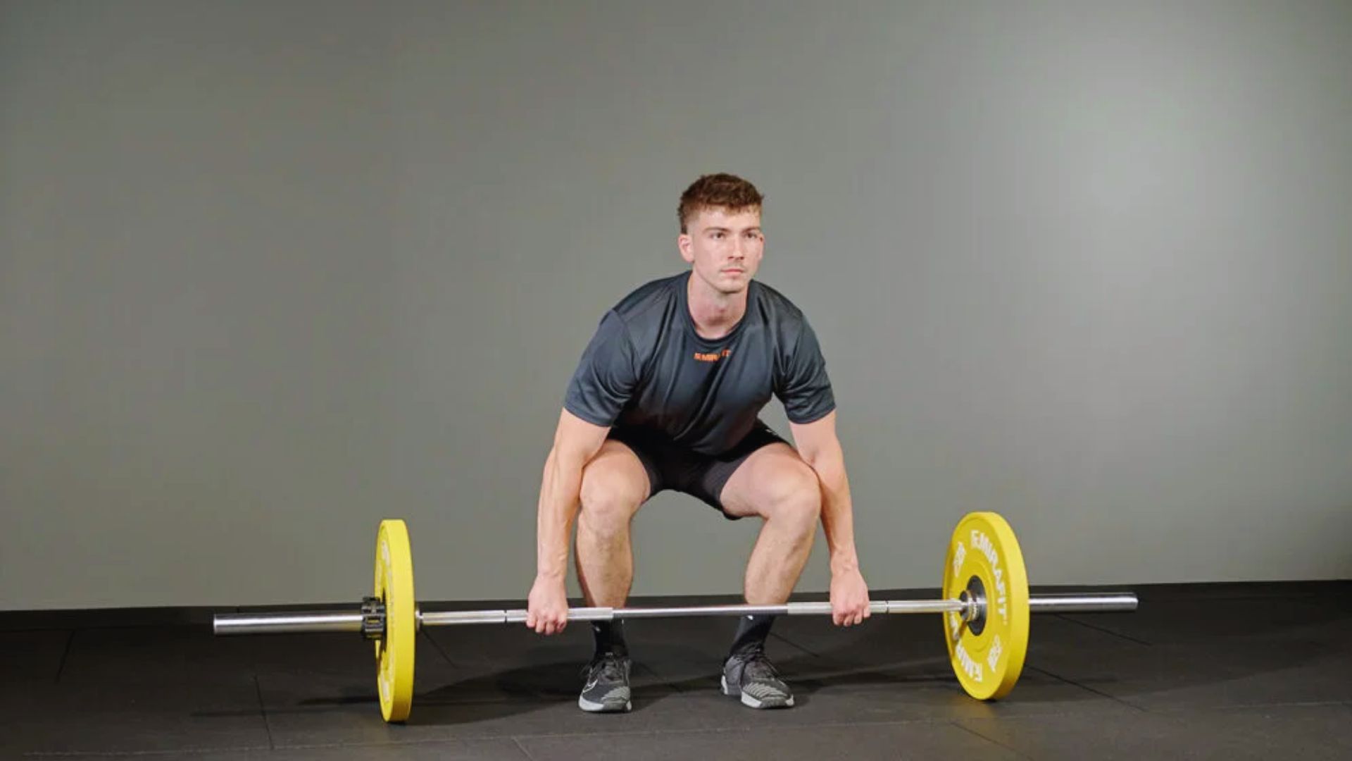 A man squats while lifting a yellow barbell, focusing on his strength training exercise.