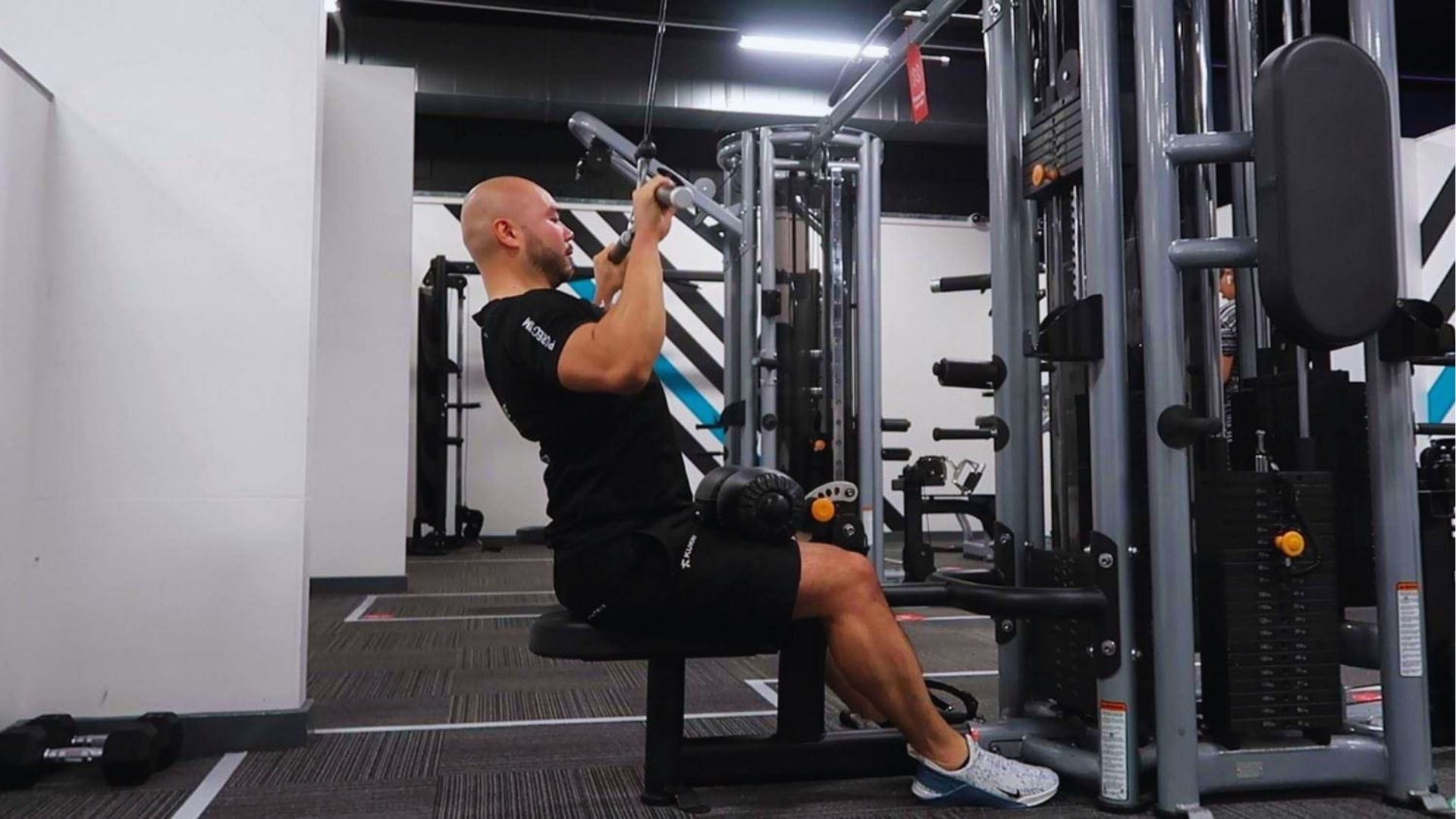 A person in a gym is performing a seated lat pulldown on a machine. They are focused and appear determined, with exercise equipment in the background.