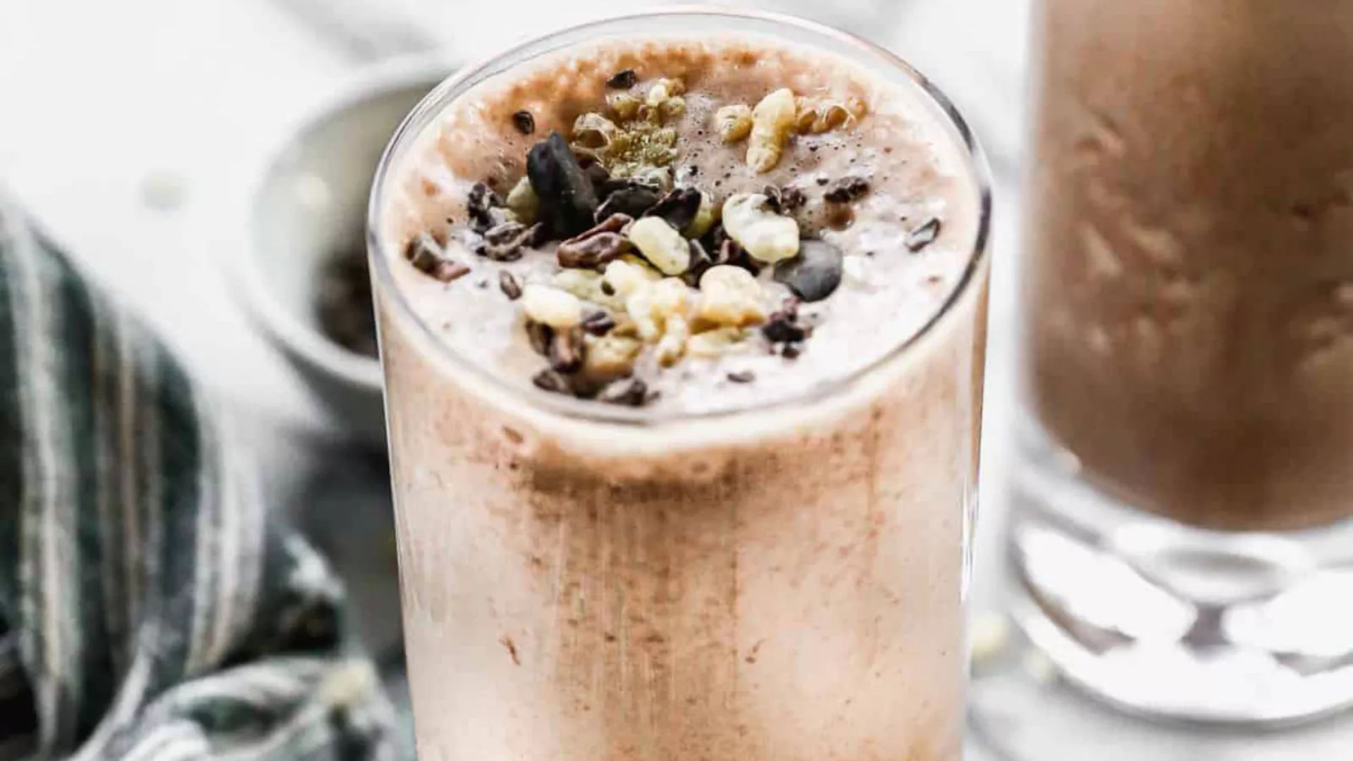 Two glasses of chocolate milk topped with a mix of nuts and seeds, placed on a wooden table.