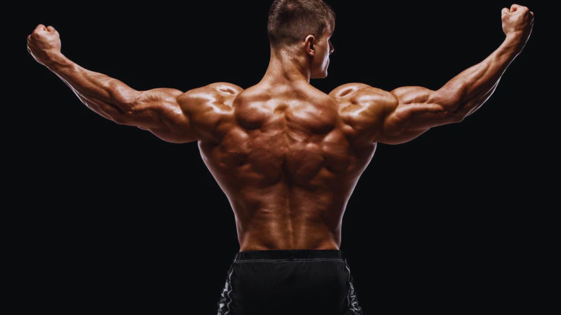 Bodybuilder flexing his muscular back and arms in a powerful pose against a dark background, showcasing strength and dedication to fitness.