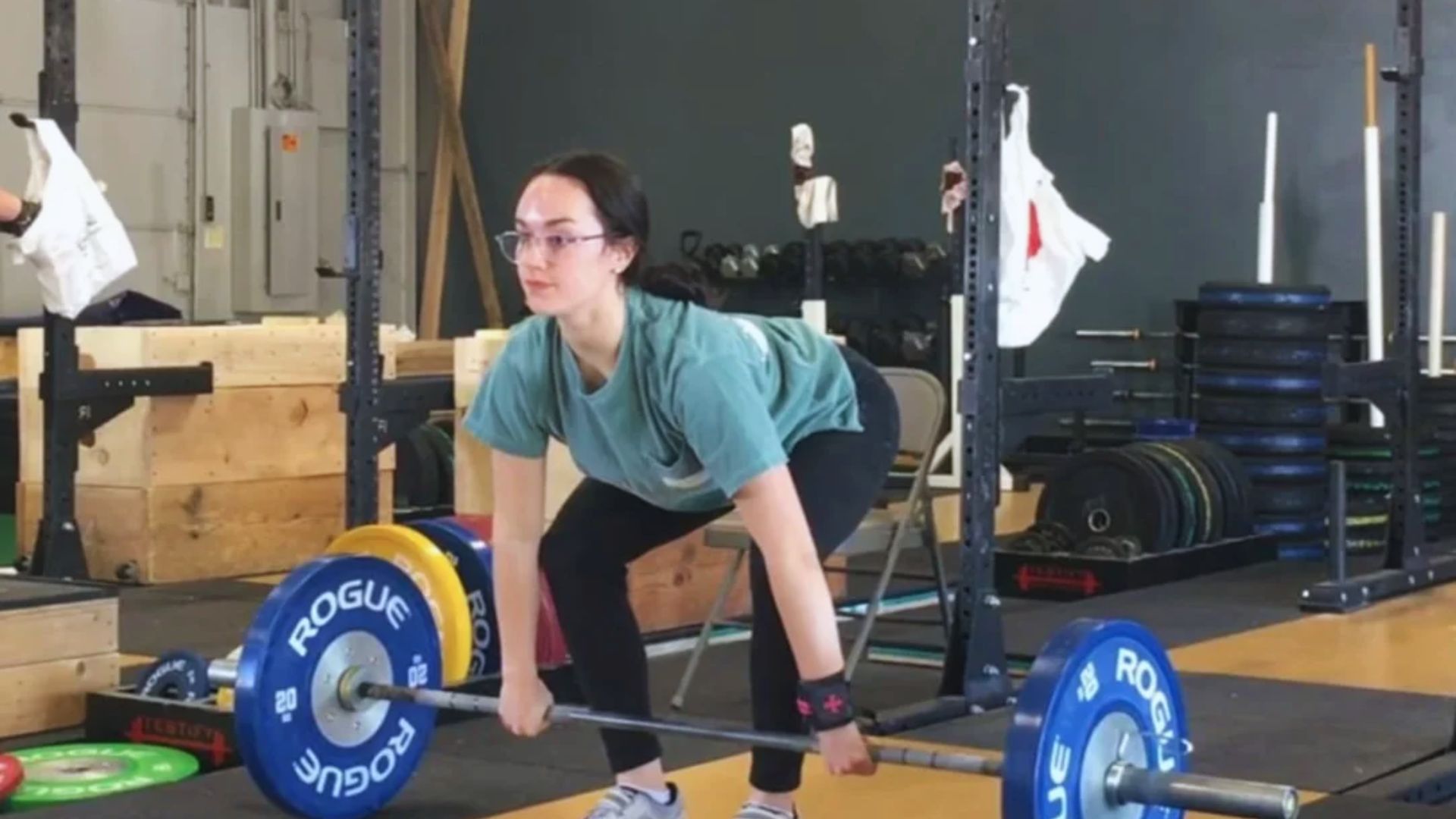 A woman squats with a barbell on her shoulders in a gym, focusing on her form and strength training.