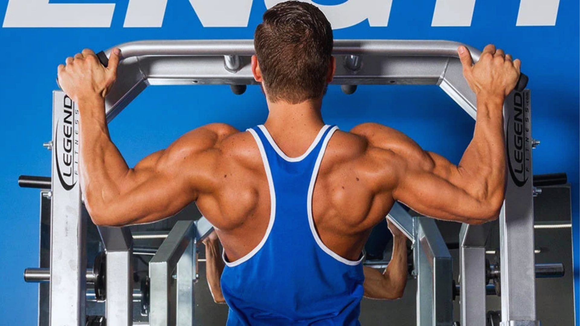 Man in blue tank top performs a pull-up on gym equipment. His muscular back is highlighted against a blue background, conveying strength and focus.