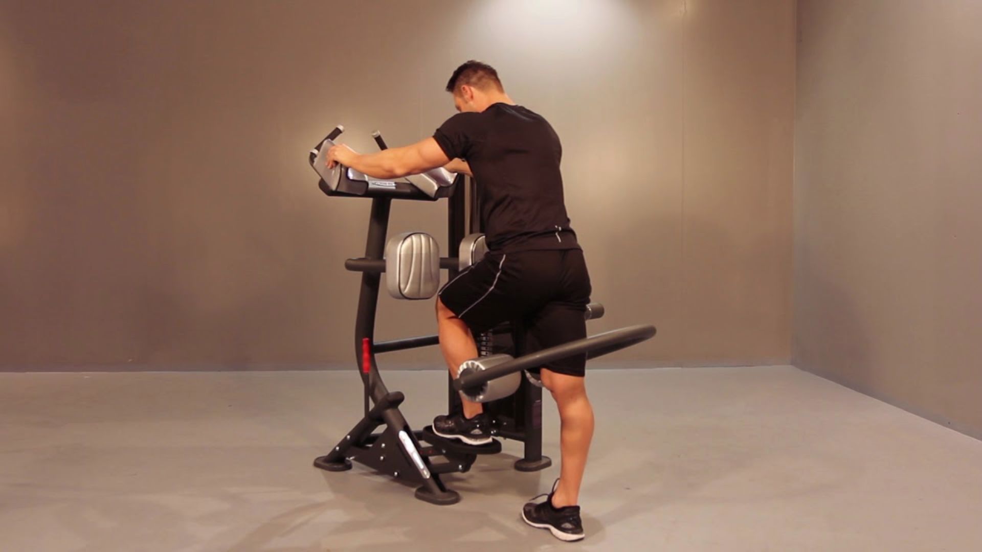 A man in athletic wear uses a gym hip abductor machine in a minimalist, well-lit room, focusing on exercise. The scene conveys determination and fitness.