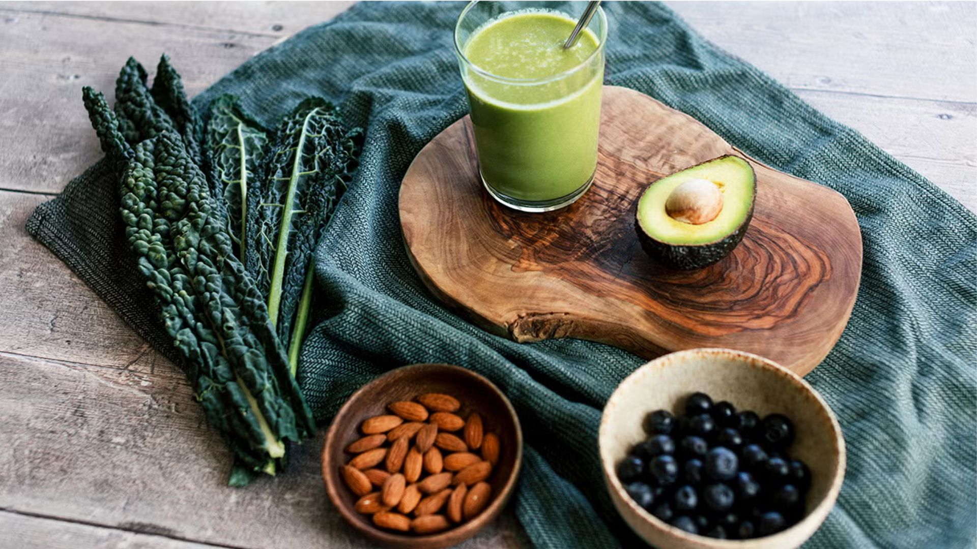 Green smoothie with avocado, kale, almonds, and blueberries on a rustic wooden table.