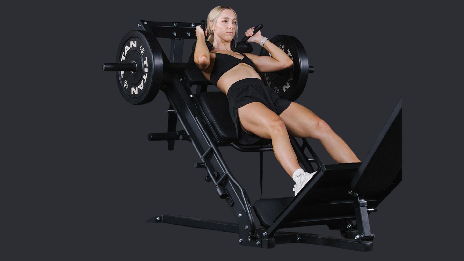 Woman in a black workout outfit using a leg press machine, appearing focused and determined. She is mid-workout in a gym environment.