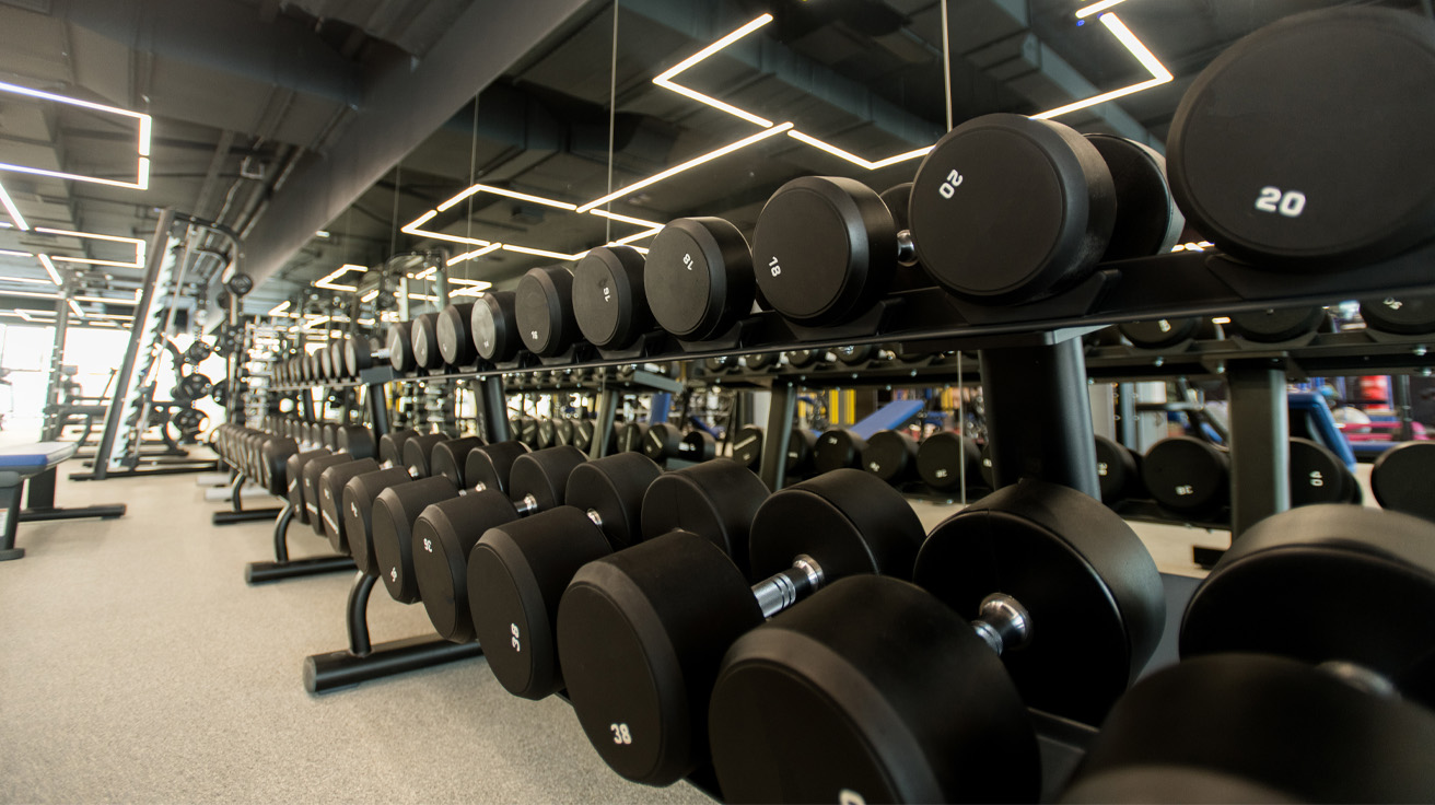 Rows of dumbbells in a modern gym, reflected in mirrors. The sleek, organized space conveys a focused and energetic atmosphere.
