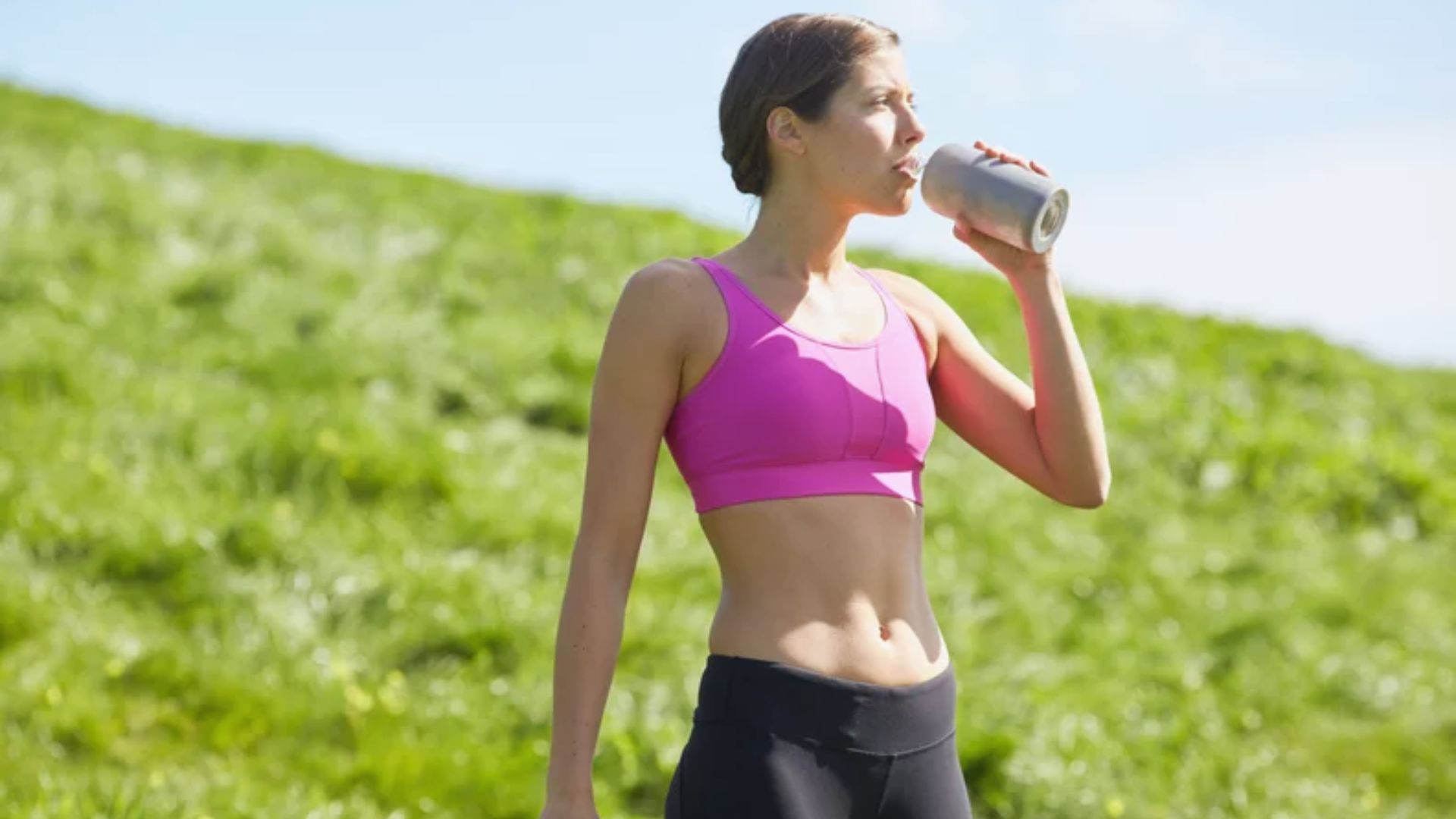 A woman in a sports bra drinks from a water bottle, showcasing an active lifestyle and fitness focus.