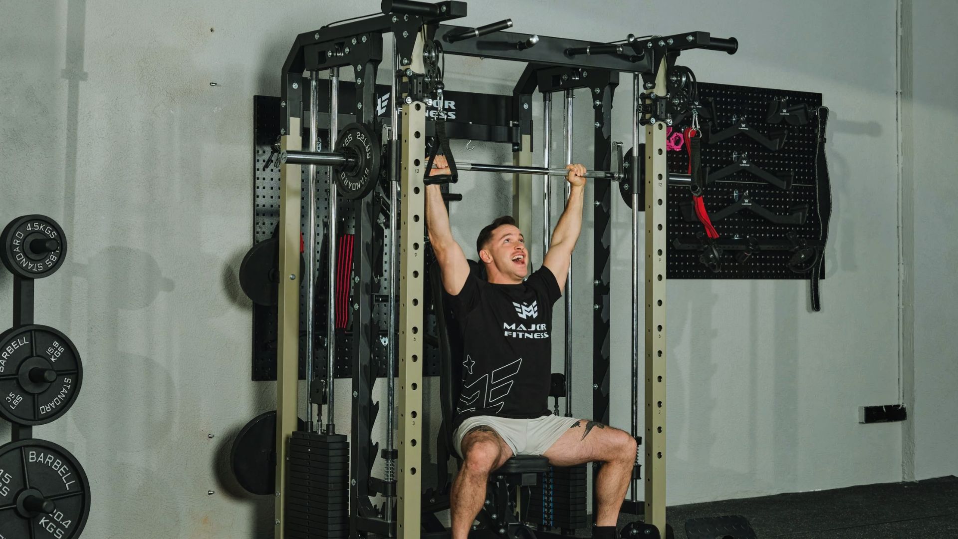 A person exercises in a gym, smiling while using a pull-down machine. Weights and equipment are visible, creating a focused, energetic atmosphere.