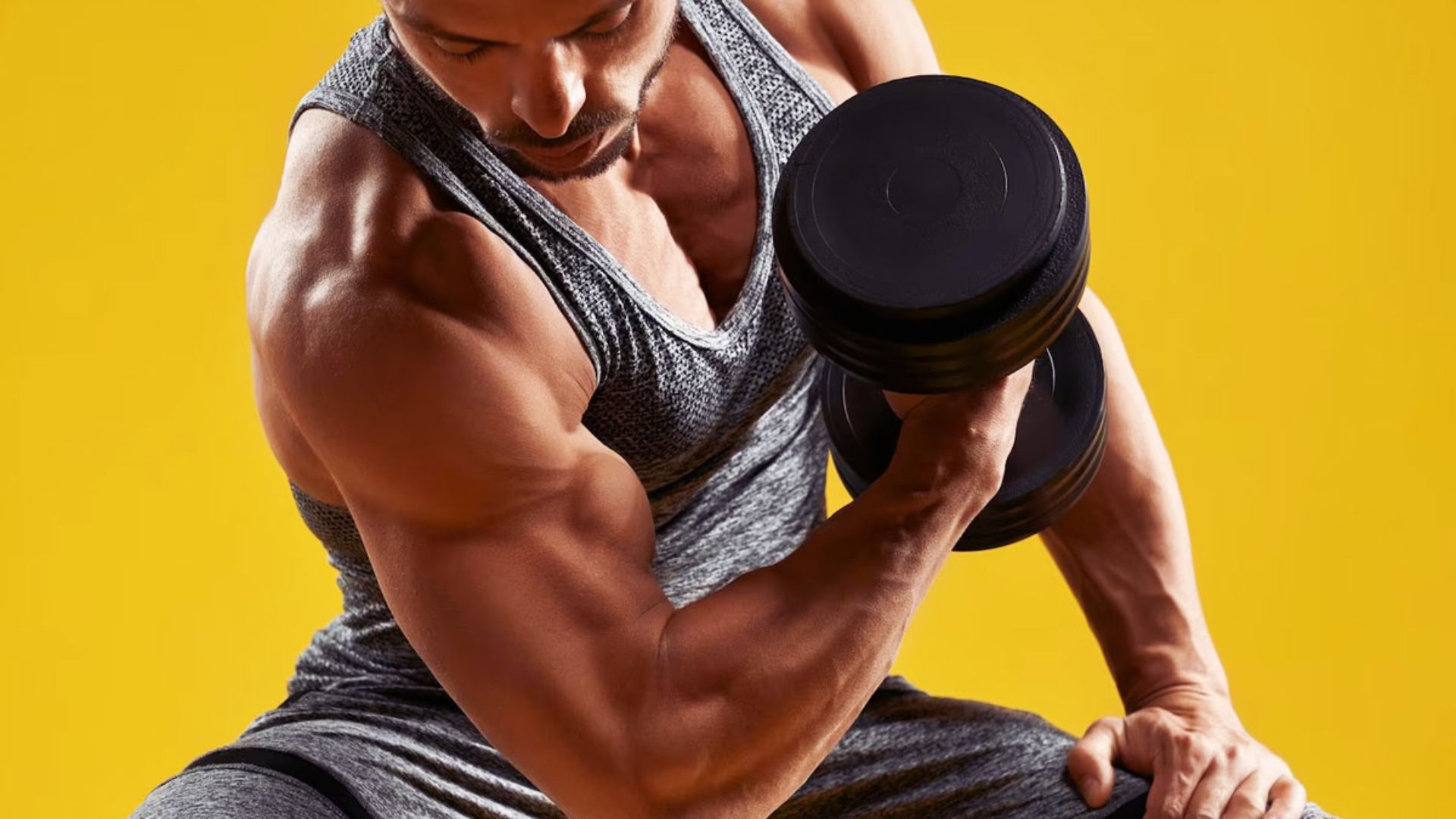 Man in gray athletic wear performs bicep curls with a dumbbell against a bright yellow background, conveying focus and strength.