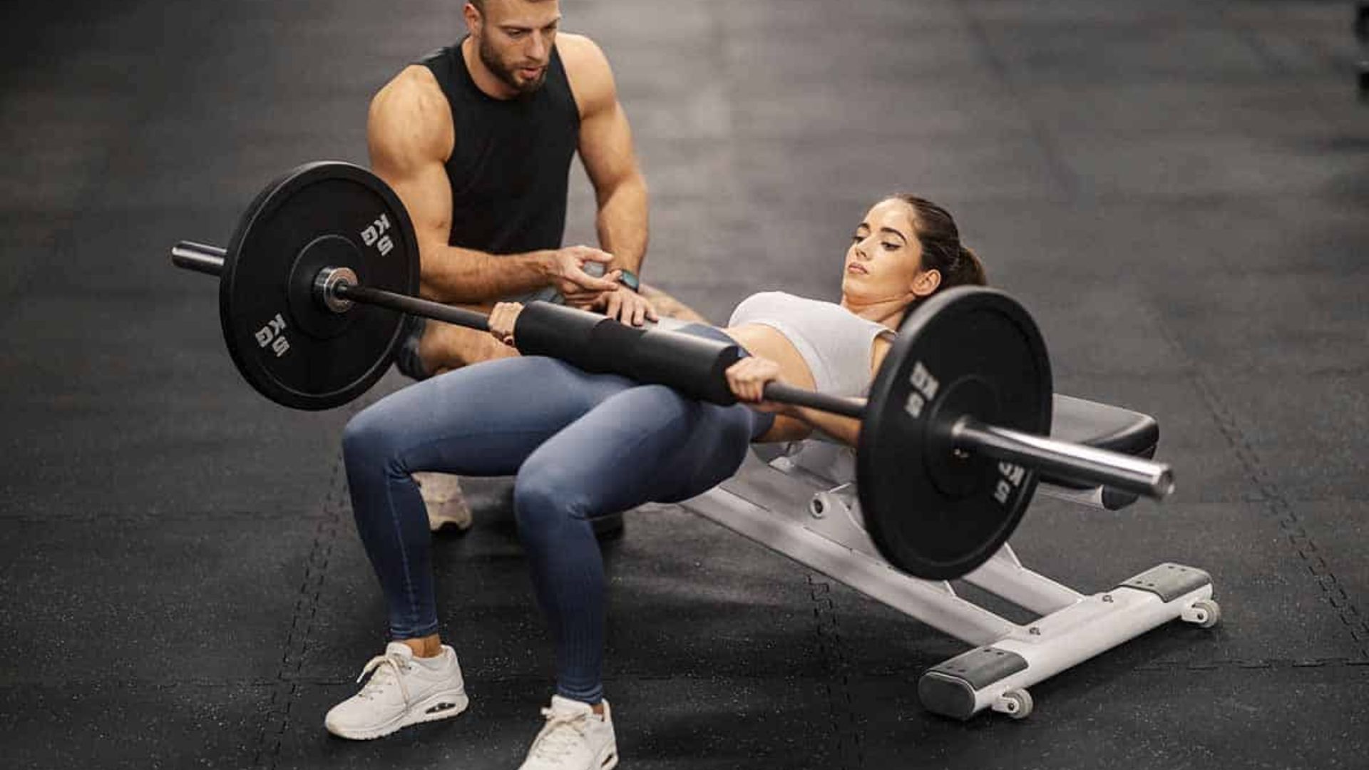 A man and woman are exercising together on a workout bench in a gym setting.