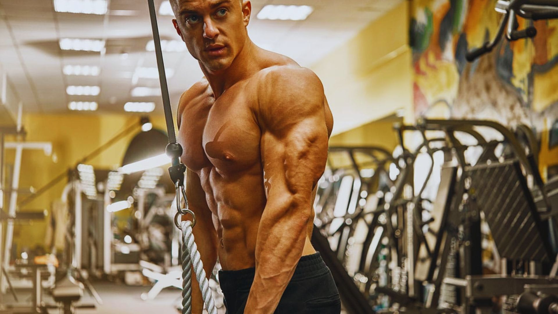 A man performs a pull-up on a bar in a gym, showcasing strength and focus during his workout.
