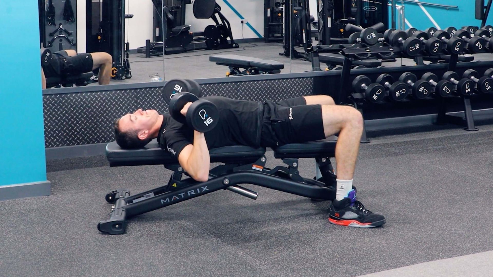 Man lifting dumbbells on a bench in a gym, surrounded by equipment and mirrors, focused on strength training