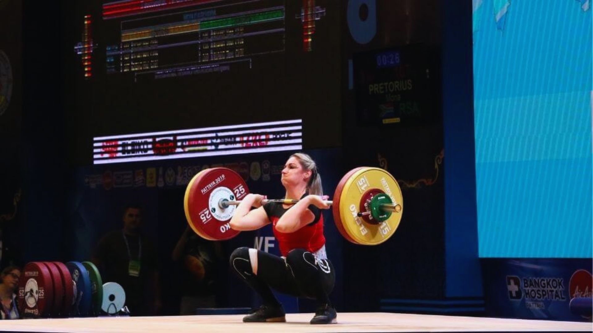 A woman squats on a platform, lifting a barbell with focused determination.