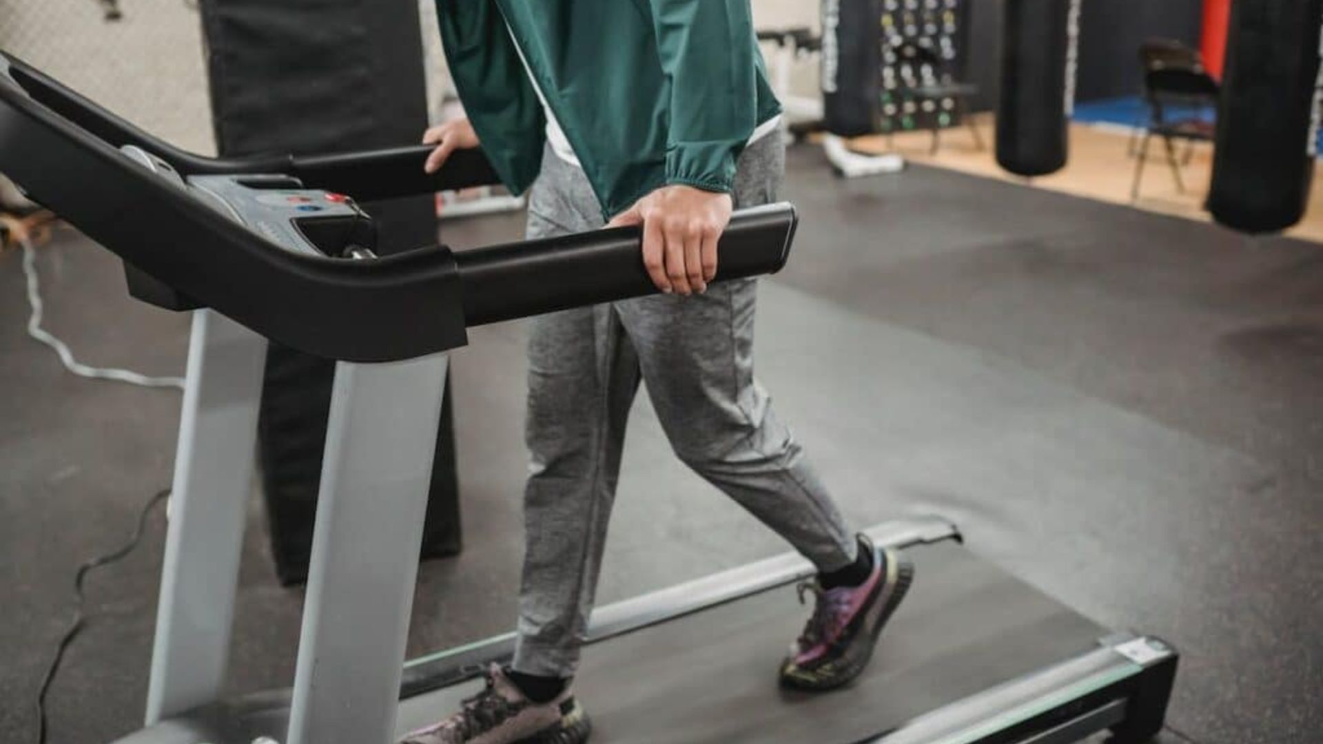 A man exercises on a treadmill in a gym, focused on his workout amidst various gym equipment.
