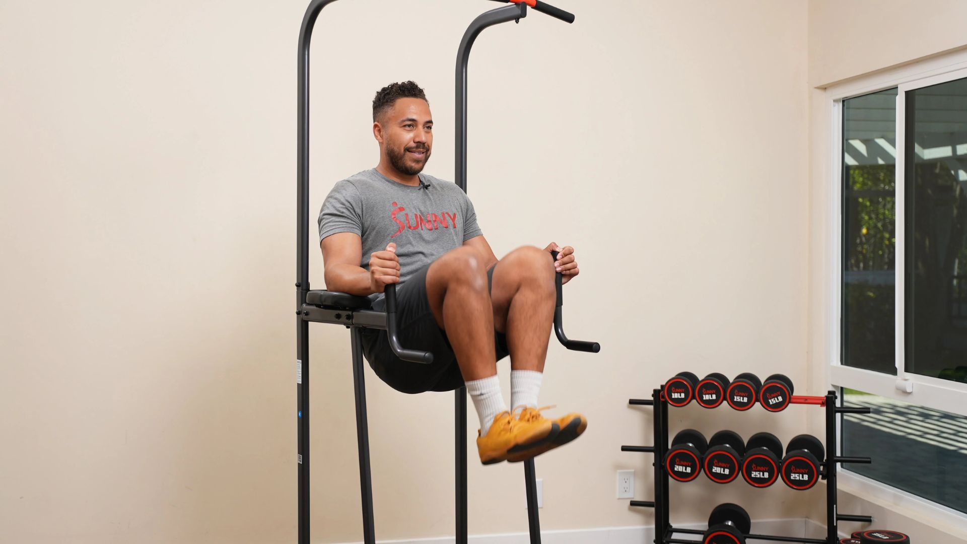 A man sits on a pull-up bar in a gym, demonstrating strength and balance during his workout routine.