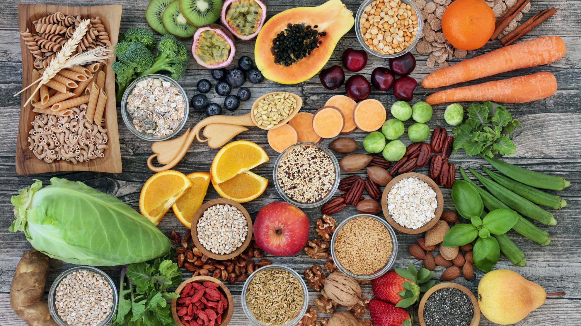 A vibrant display of healthy foods on a wooden surface, including fruits, vegetables, grains, and nuts, arranged neatly to convey variety and nutrition.