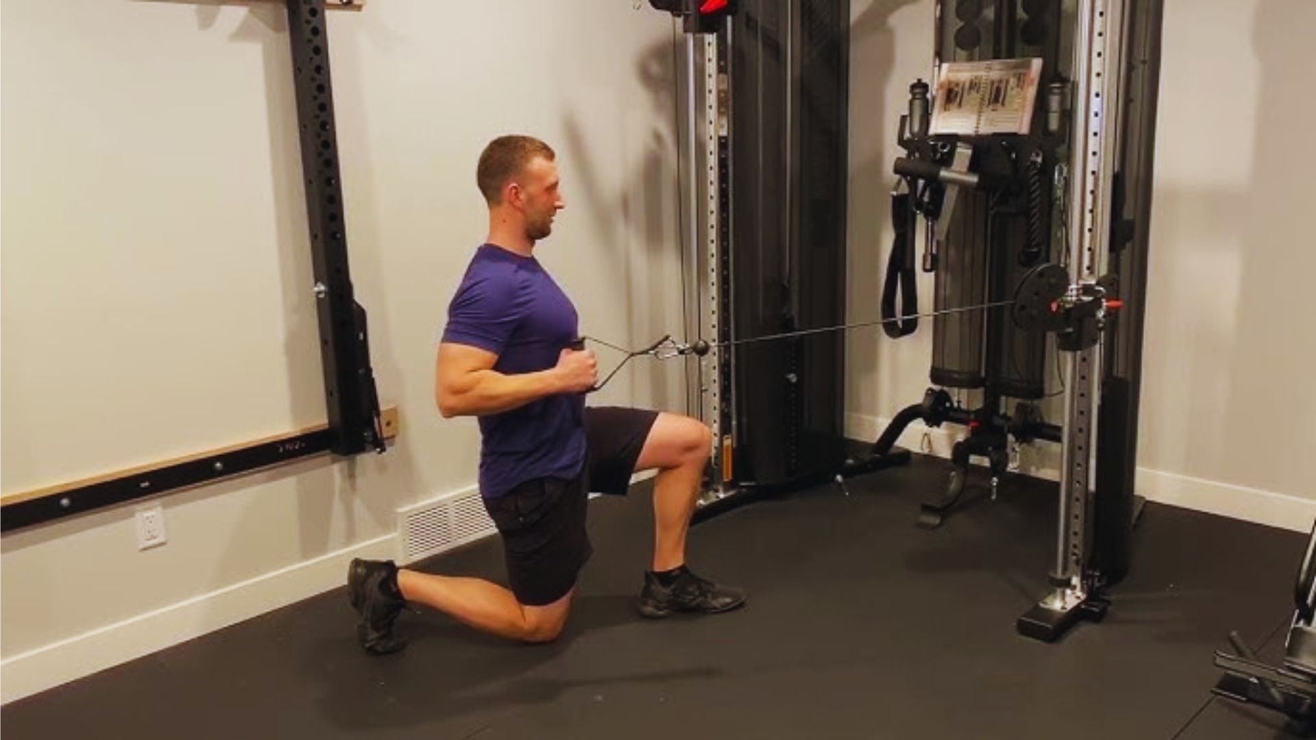 A man in a blue shirt performs a kneeling cable row in a gym, showcasing strength and focus. The room is equipped with modern fitness machines.