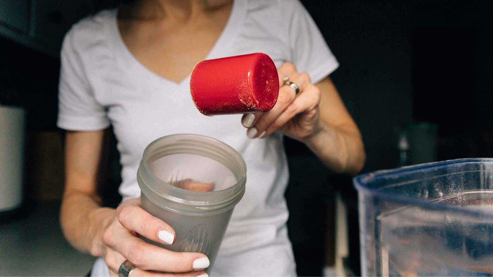 A woman pours a vibrant red liquid into a blender, preparing to mix ingredients for a smoothie or sauce.
