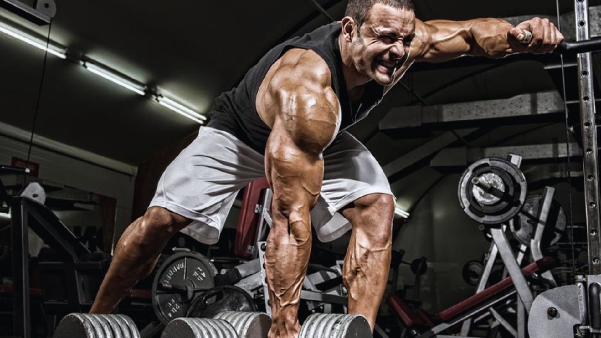 A muscular man in a gym intensely lifts heavy weights. His expression shows determination and effort, highlighting his strength and focus amidst gym equipment.