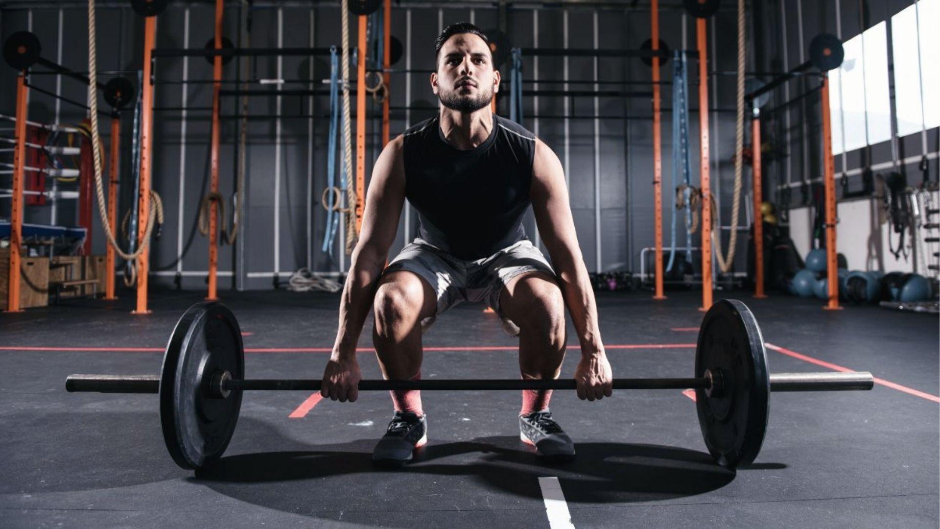 Man in gym grips barbell mid-deadlift, back day bro split starts with heavy compound pull