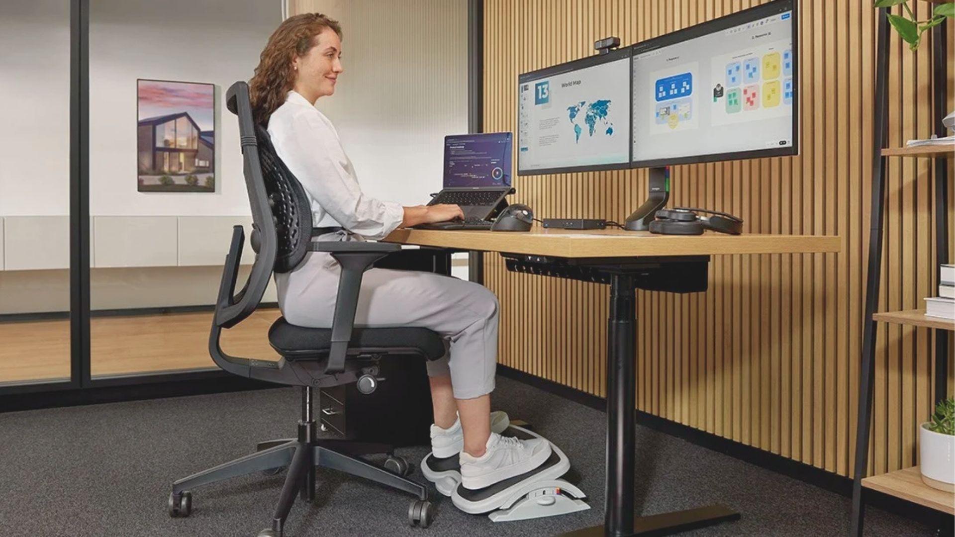 Woman sitting with good posture at a standing desk using dual monitors and an ergonomic chair.