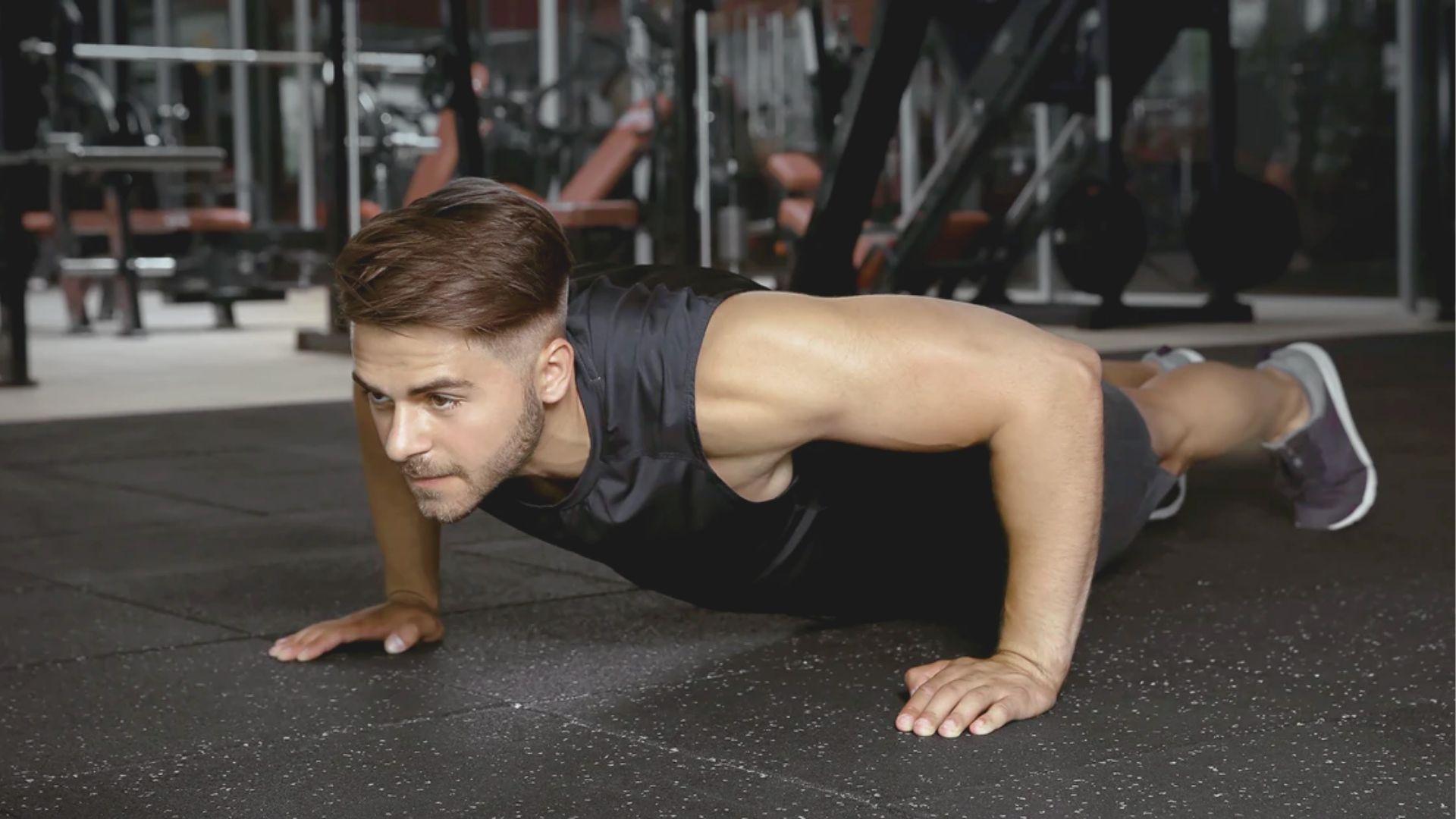 Man in dark t-shirt performing the bottom hold of a negative push up on gym flooring.