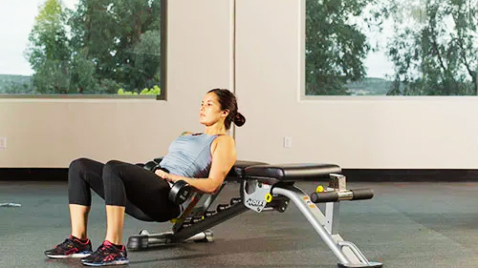 Woman doing a weighted glute bridge with dumbbells, using a slant board adjustable bench for support.
