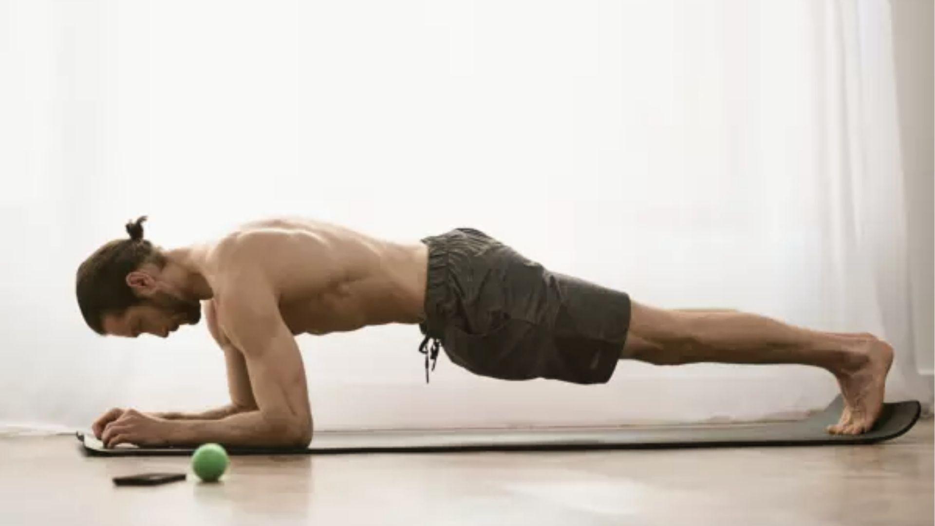 Fit man holds forearm plank on yoga mat indoors building core stability for day 1 calisthenics