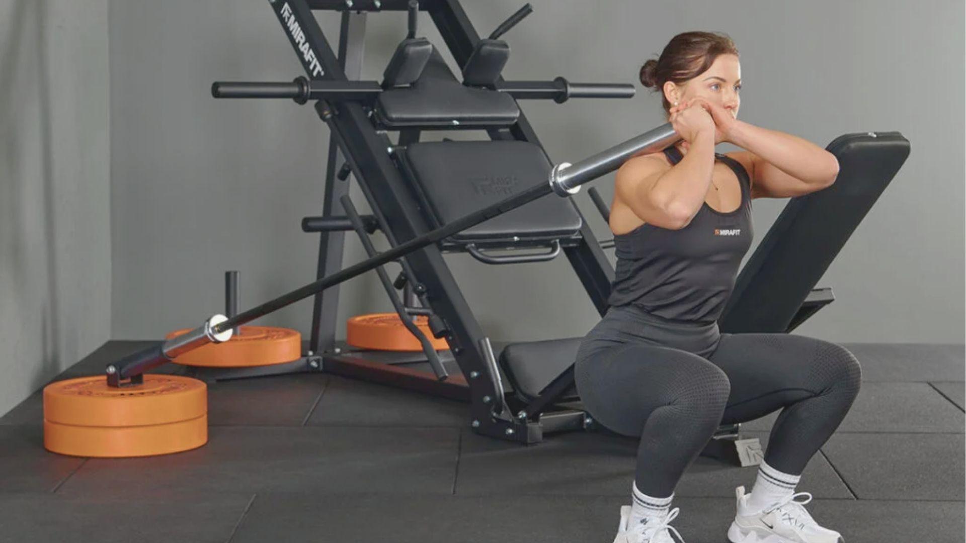 A woman in a black tank top performs a deep landmine squat, holding the barbell end at chest height.