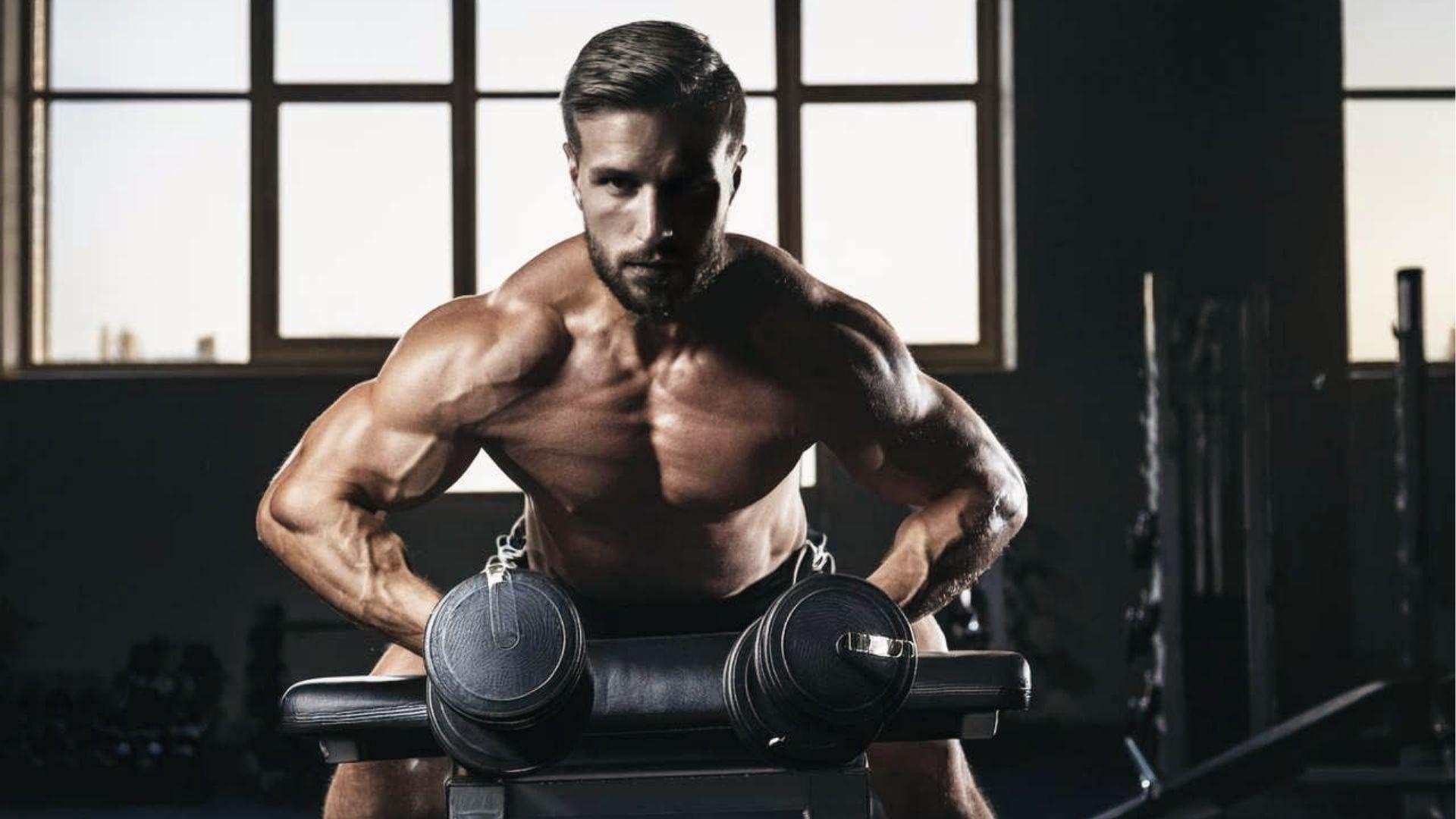 Muscular man does dumbbell spider curls lying on incline bench, elbows forward, biceps fully engaged.