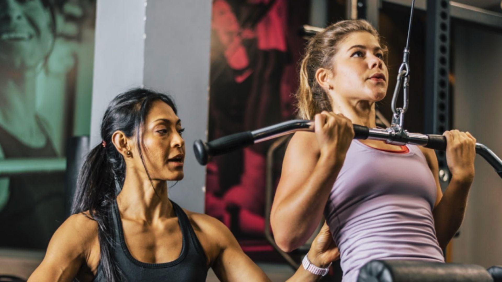 Two women performing strength training exercises together in a gym, completing a workout set.