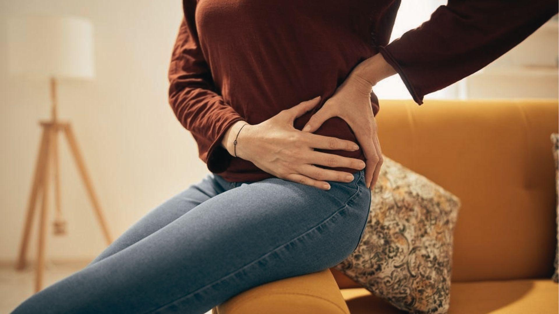 Older adults hold their hips while sitting on bed, showing discomfort from hip pain when seated.