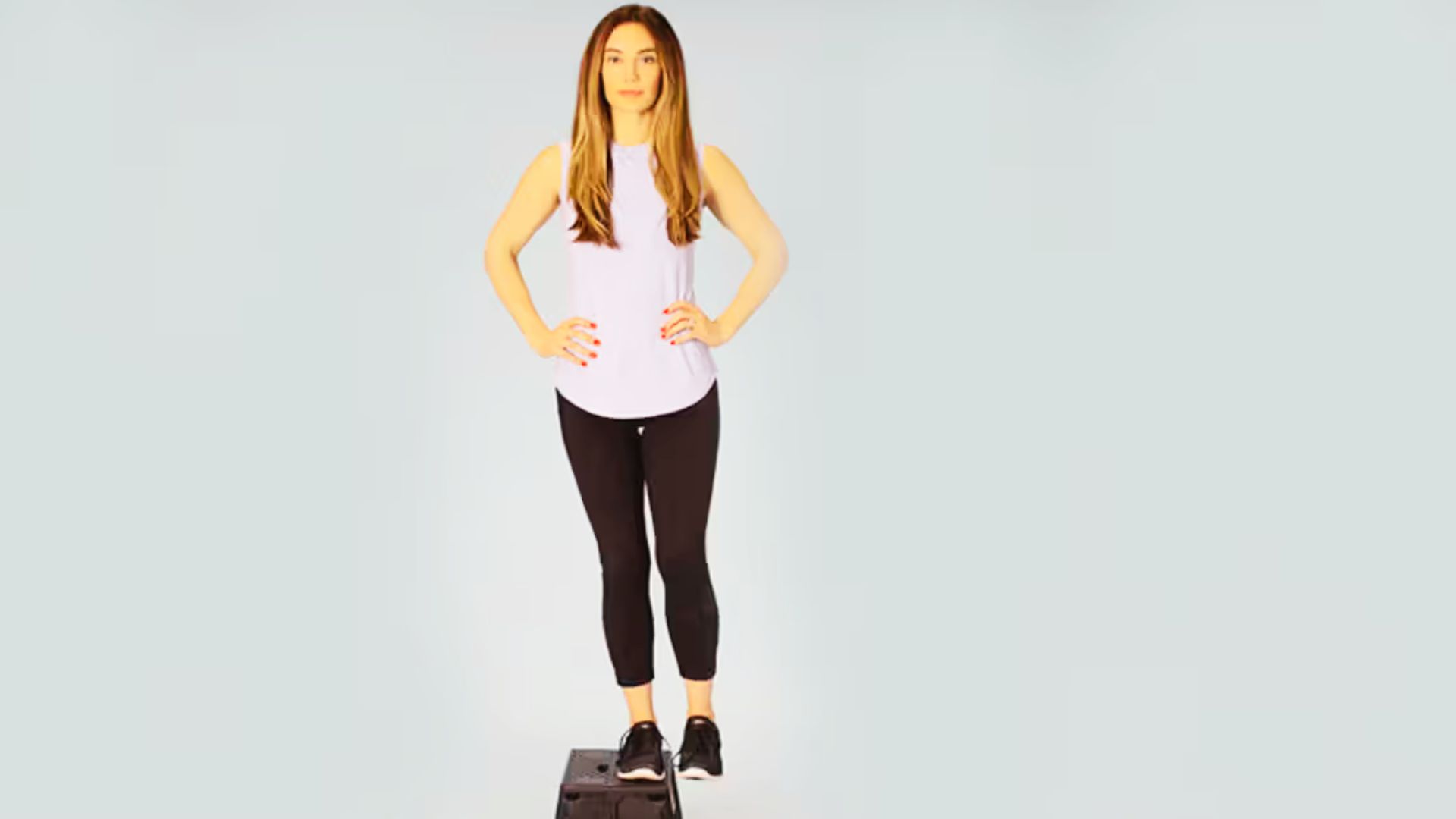 A woman stands upright on an exercise step with both feet, preparing for a heel-uplifted step down.