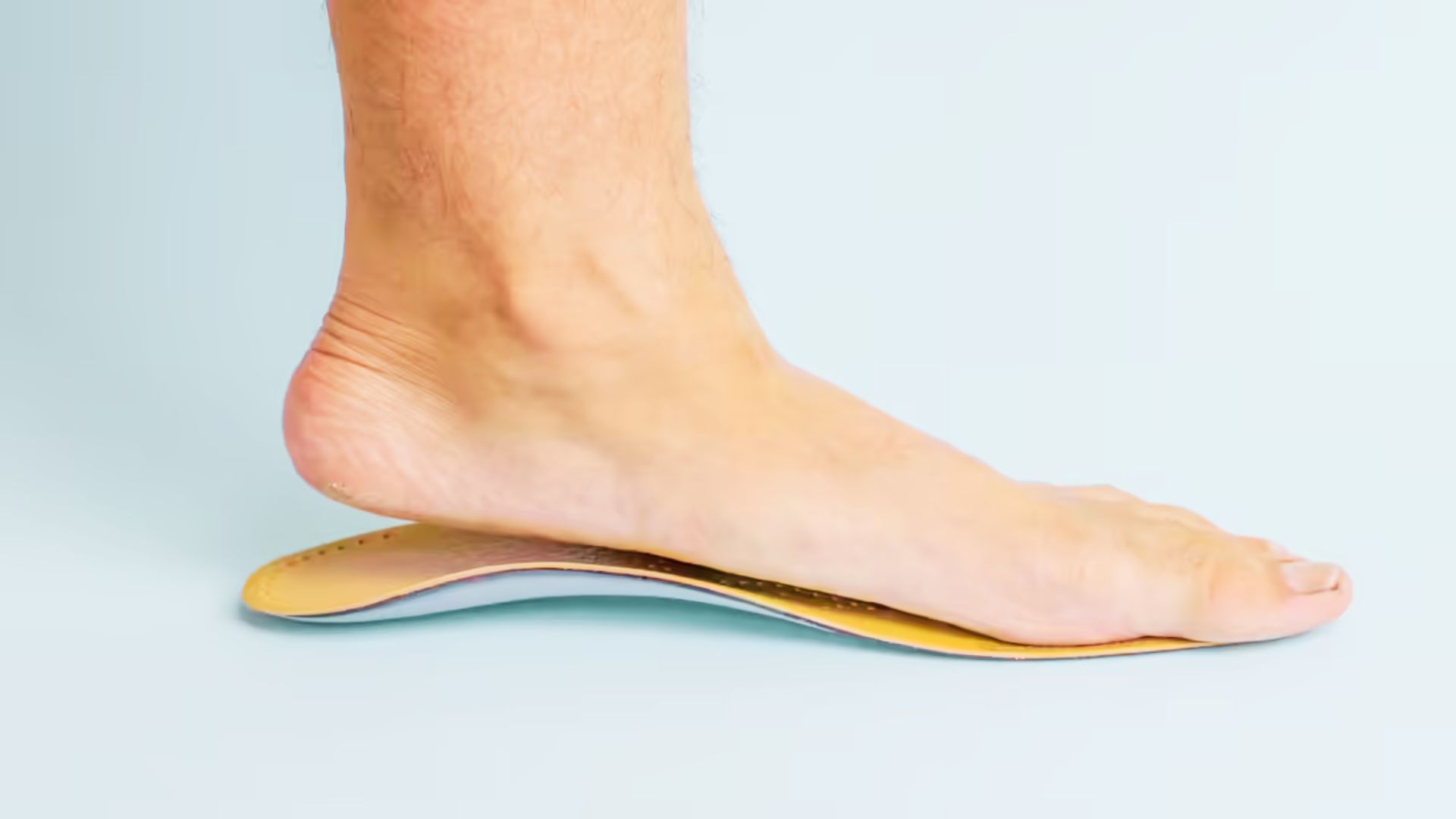 Side view of a bare foot stepping onto a contoured yellow orthotic insole against a light blue background.