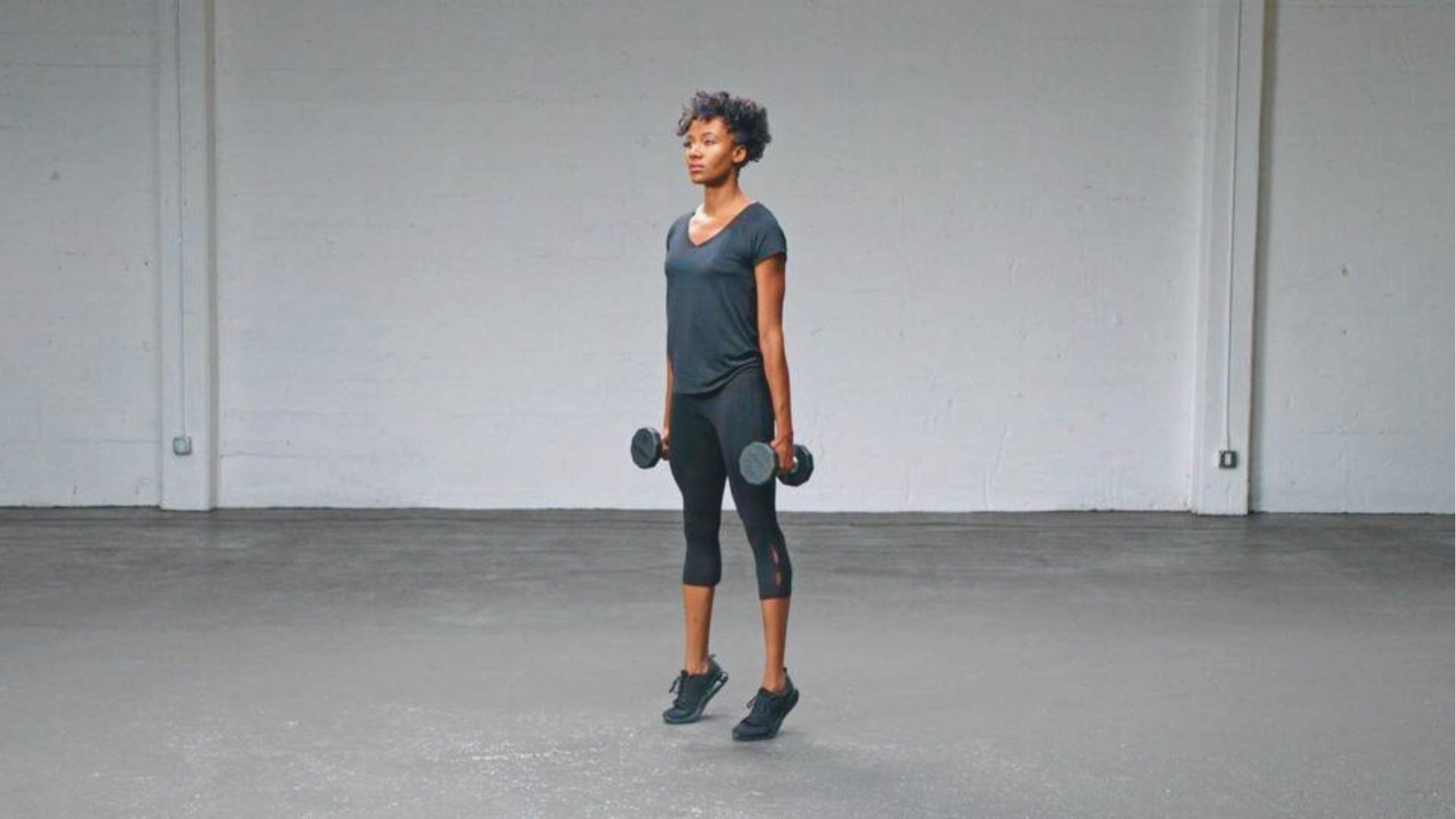 Woman holding dumbbells while rising onto her toes for weighted standing calf raises.
