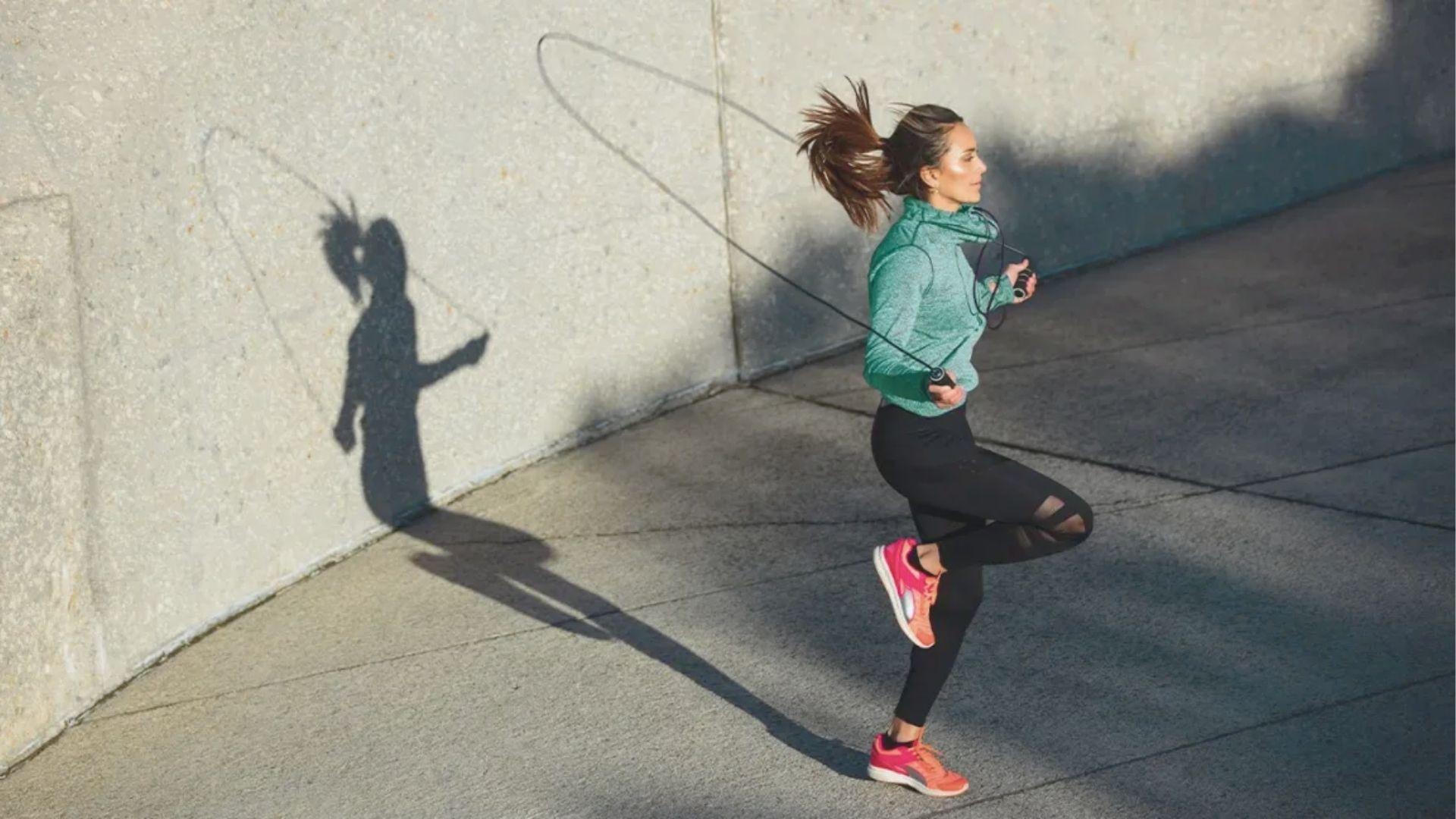 Woman jump-roping outdoors against a concrete wall, casting a shadow.