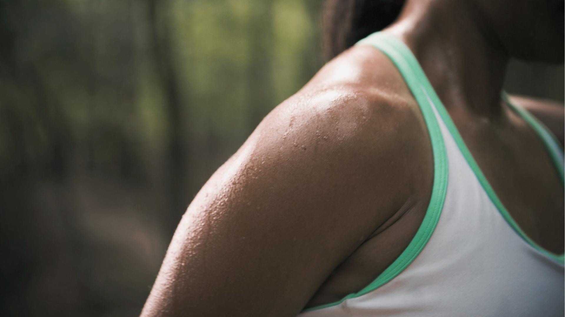 Close-up of woman’s sweaty shoulder and upper back in mint-trim tank top during outdoor trail run.