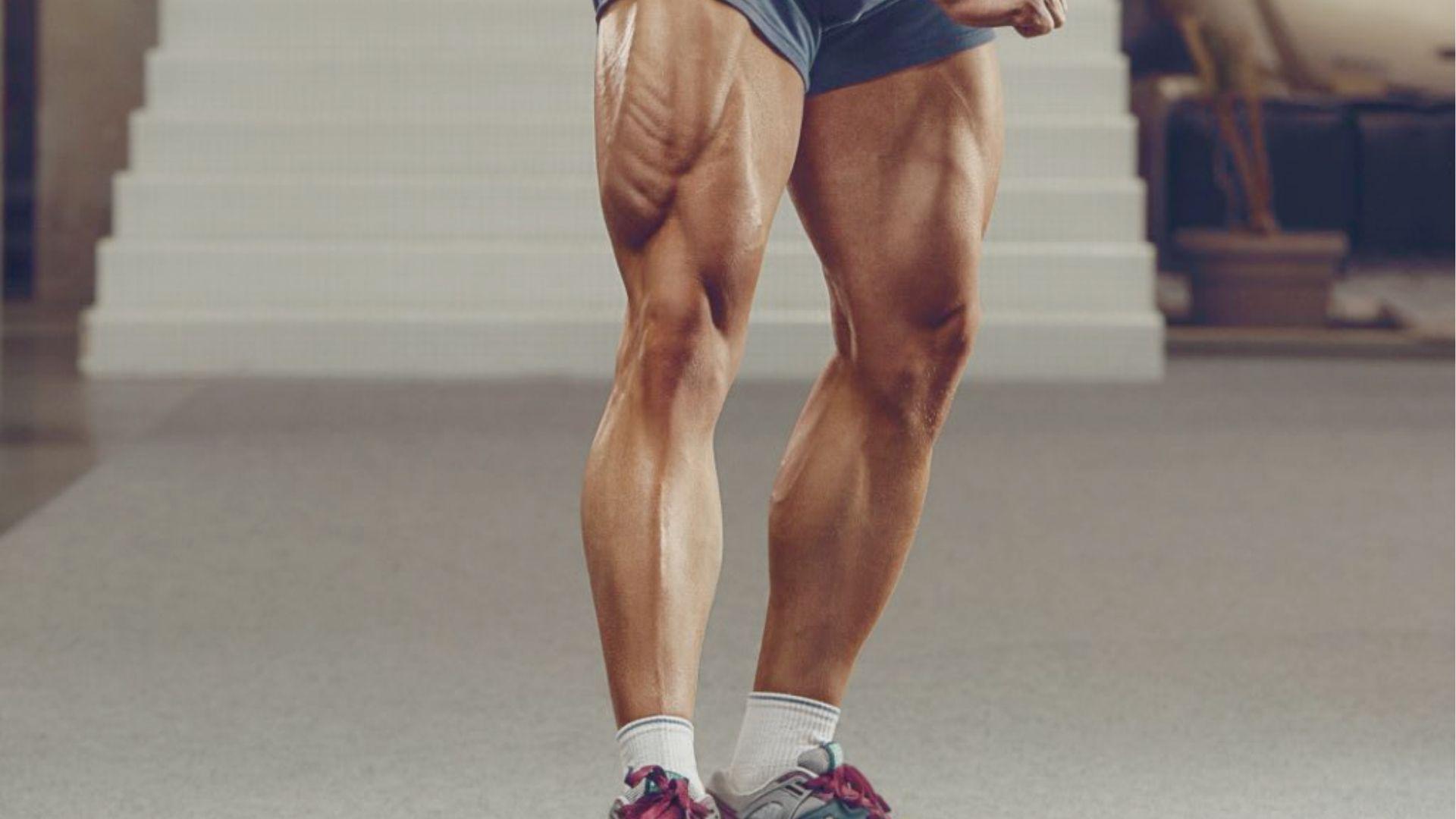 Athlete’s legs with defined quads, hamstrings, and calves standing in a gym setting.
